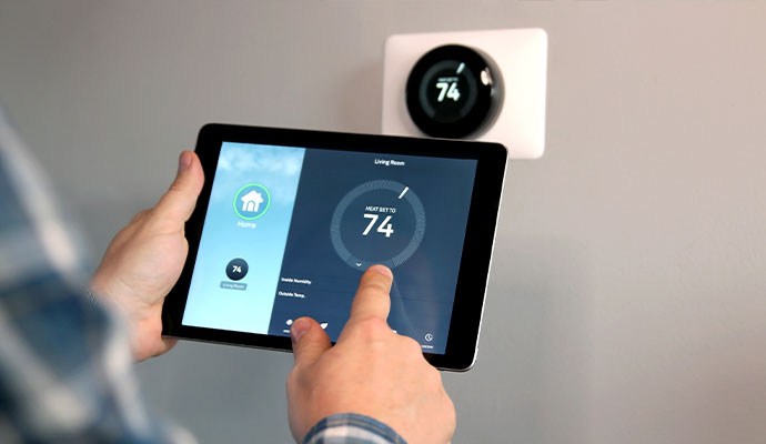Person using a tablet to adjust the temperature on a wall-mounted smart thermostat